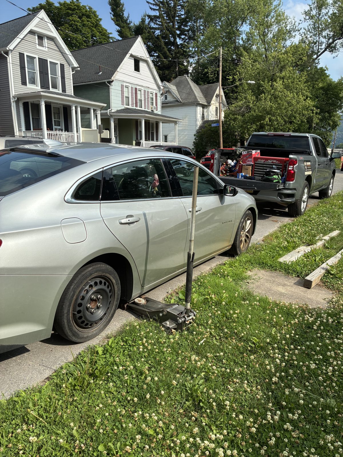Vagabond mobile mechanic servicing a car jacked up curbside with the work truck parked behind
